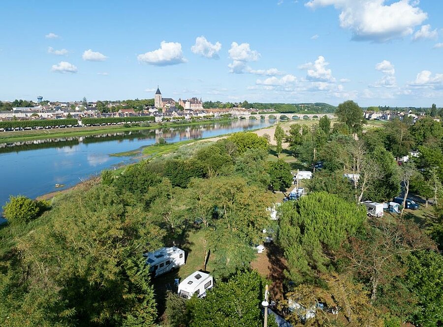Vue aérienne d’un camping arboré au bord de la Loire, avec Gien et son pont en arrière-plan