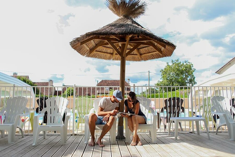 Jeune couple en pleine détente sous un parasol en bord de piscine dans un camping pas cher, à la recherche du meilleur rapport qualité-prix.