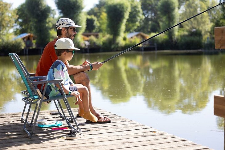Pêche père et enfant à l’étang dans un camping nature Père et enfant pêchant à l’étang d’un camping nature, moment calme en pleine nature bénéfique pour le bien-être.